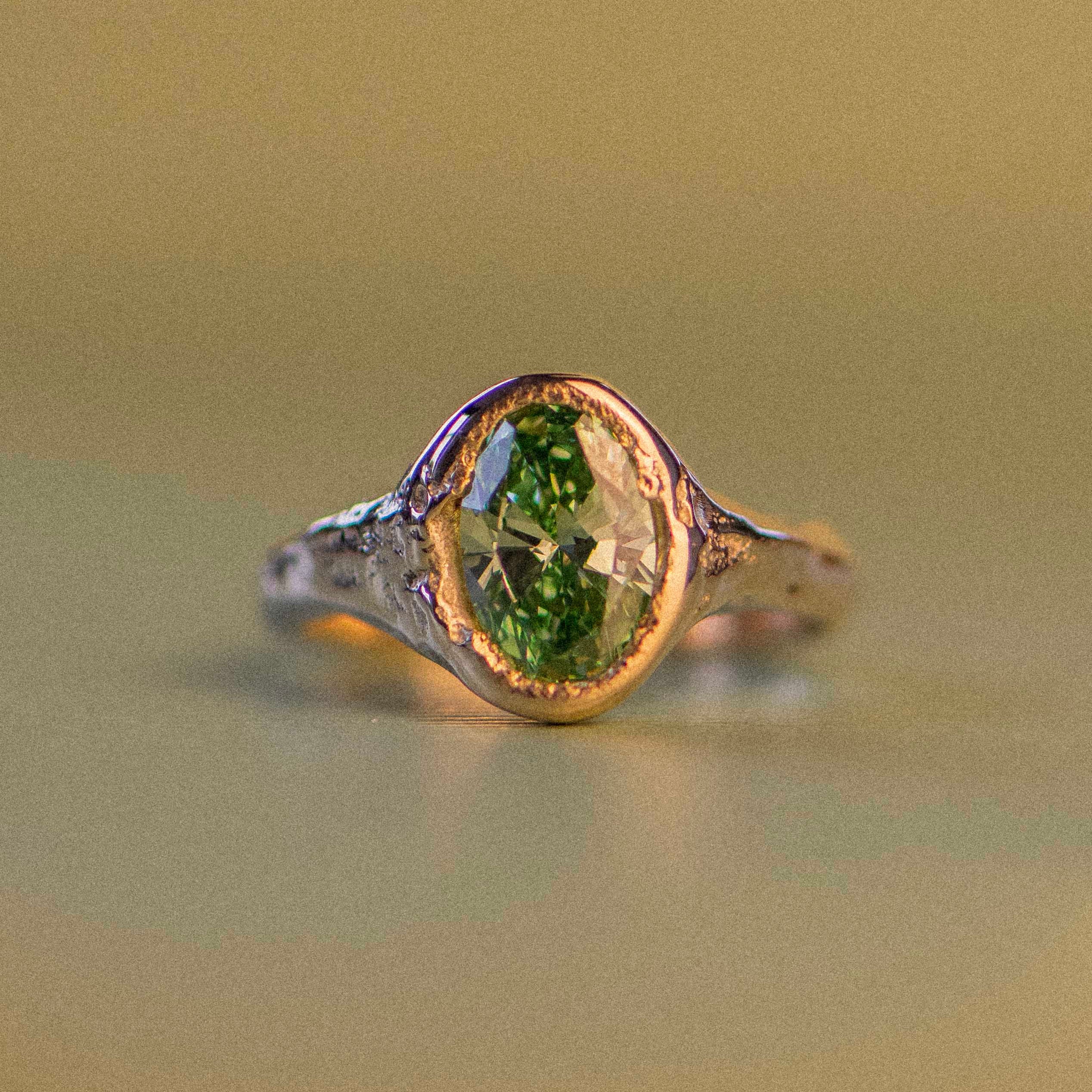 Gold ring with a green diamond on a beige background